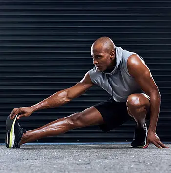 Male athlete, exercise and stretching leg with hand for sports, workout and fitness in gym. Healthy man, challenge and cardio routine for wellness, muscle and strength training for mental wellbeing