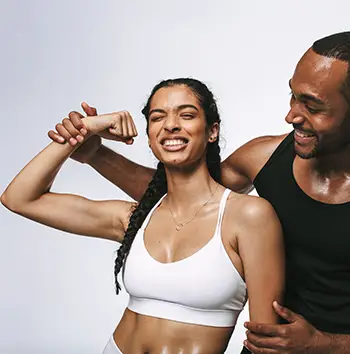 Cheerful fitness woman having fun showing biceps standing with male athlete. Fitness couple sharing happy moments after workout.